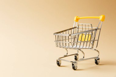Süpermarket bakkal itme sepetinin siyah jantlar ve tutamacı üzerinde bej arka plan izole sarı plastik öğelerle birlikte alışveriş için kapatın. Alışveriş kavramı. Kopya alanı reklam için