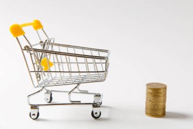 Süpermarket bakkal itme sepeti ile sarı plastik saplı sonraki beyaz arka plan üzerinde izole altın sikke yığını için alışveriş için kapatın. Alışveriş, para kavramı. Kopya alanı reklam için