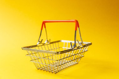 Metal alışveriş sepetinin kaldırdı kolları ve Sarı zemin üzerine izole turuncu plastik elemanları süpermarkette alışveriş için kapatın. Alışveriş kavramı. Kopya alanı reklam için