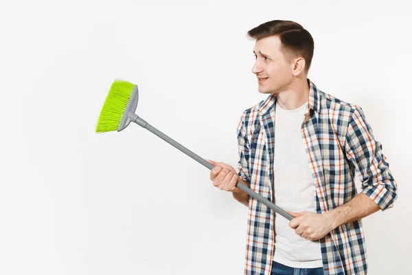 Jovem estranho divertido governanta homem em xadrez camisa segurando e varrendo com vassoura verde isolado no fundo branco. Homem a fazer tarefas domésticas. Espaço de cópia para propaganda. Conceito de limpeza . — Fotografia de Stock