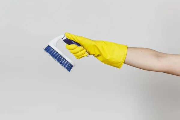 Primer plano de la mano femenina en guantes amarillos horizontal sostiene cepillo blanco con fibras duras para la limpieza con elementos azules aislados sobre fondo blanco. Concepto de artículos de limpieza. Copiar espacio para anuncio —  Fotos de Stock