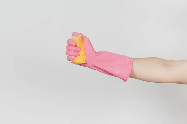 Närbild av kvinnlig hand i rosa handskar håller och kramar gul-orange svamp för rengöring och diska isolerad på vit bakgrund. Rengöring leveranser koncept. Kopiera utrymme för reklam — Stockfoto