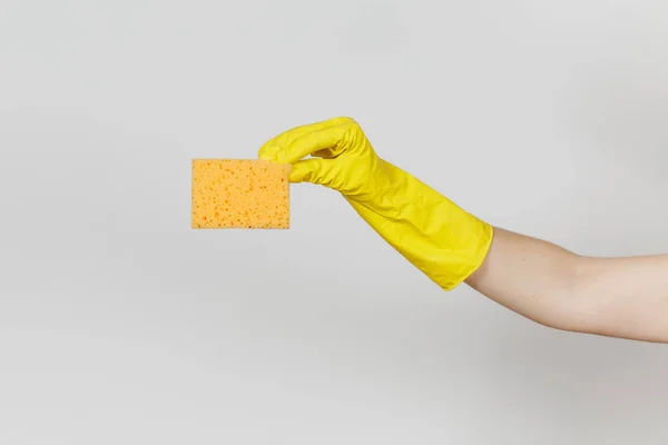 Close up de mão feminina em luvas amarelas horizontal detém esponja amarelo-laranja para a limpeza e lavagem de pratos isolados em fundo branco. Conceito de material de limpeza. Espaço de cópia para propaganda — Fotografia de Stock