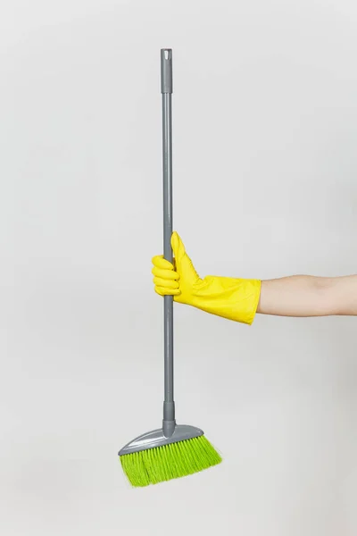 Close up of female hand in yellow gloves holds long gray broom with green villi for cleaning and sweeping isolated on white background. Cleaning supplies concept. Copy space for advertisement