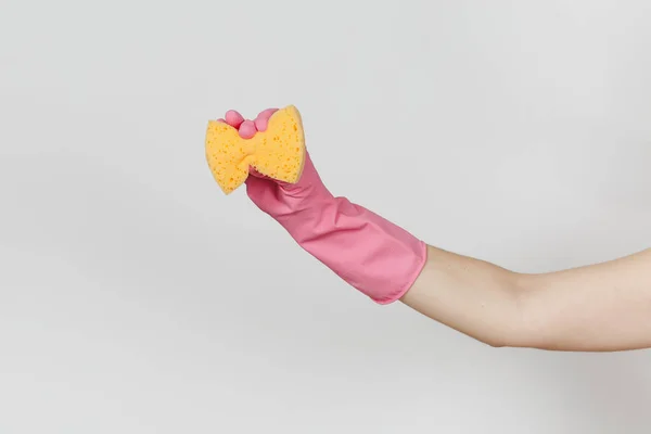 El primer plano de la mano femenina con guantes rosas sujeta y aprieta la esponja amarillo-naranja para limpiar y lavar los platos aislados sobre fondo blanco. Concepto de artículos de limpieza. Copiar espacio para publicidad — Foto de Stock