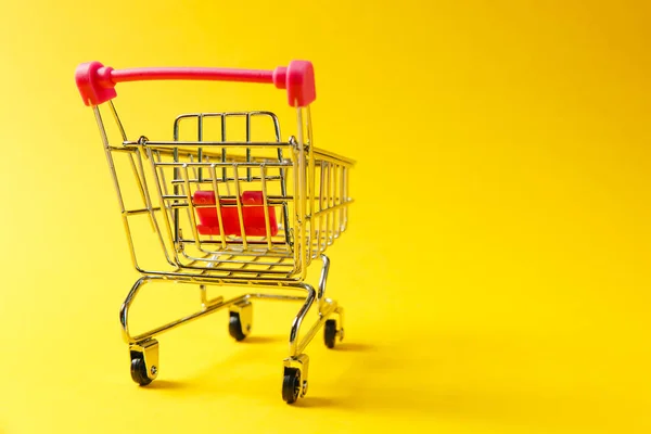 Gros plan du chariot d'épicerie de supermarché pour faire du shopping avec des roues noires et des éléments en plastique rouge sur poignée isolée sur fond jaune. Concept de shopping. Espace de copie pour la publicité — Photo