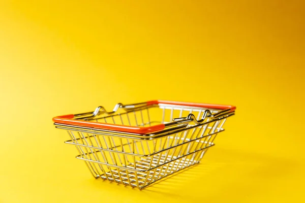 Detailní záběr z kovu s potravinami košík na nákupy v supermarketu s snížený rukojeti a oranžové plastové prvky izolované na žlutém pozadí. Koncept nakupování. Kopírovat prostor pro reklamu — Stock fotografie