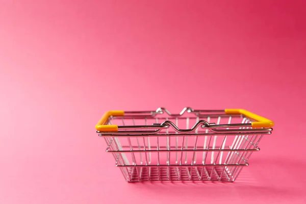 Gros plan du panier d'épicerie en métal pour faire du shopping dans un supermarché avec des poignées abaissées et des éléments en plastique jaune isolés sur fond rose. Concept de shopping. Espace de copie pour la publicité — Photo