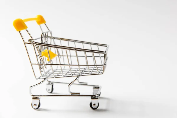 Primer plano de supermercado carrito de compras empuje con ruedas negras y elementos de plástico amarillo en mango aislado sobre fondo blanco. Concepto de compras. Copiar espacio para publicidad — Foto de Stock