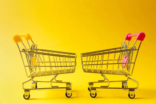 Gros plan de deux chariots d'épicerie de supermarché pour faire du shopping avec un élément jaune et rose sur la poignée en face de l'autre isolé sur fond jaune. Concept de shopping. Espace de copie pour la publicité — Photo
