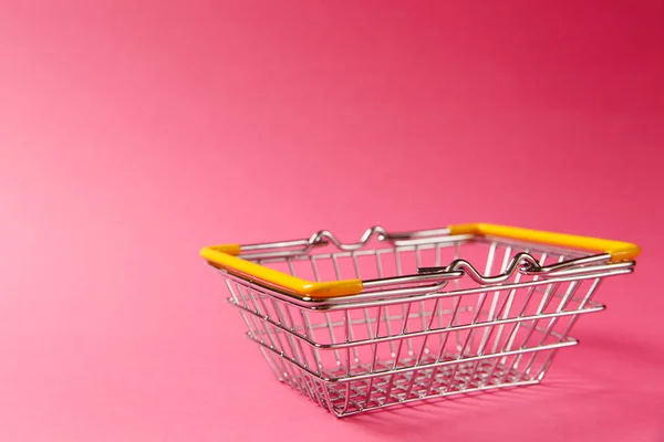 Gros plan du panier d'épicerie en métal pour faire du shopping dans un supermarché avec des poignées abaissées et des éléments en plastique jaune isolés sur fond rose. Concept de shopping. Espace de copie pour la publicité — Photo