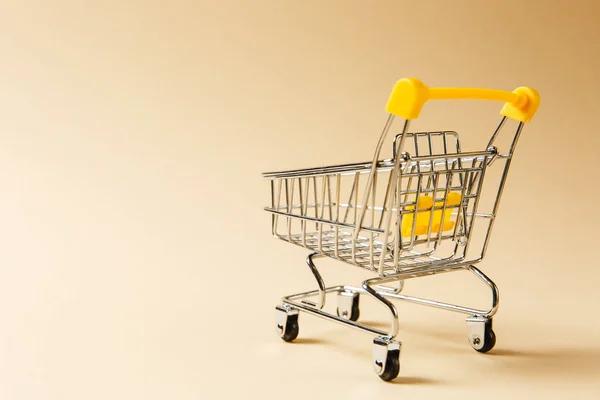 Gros plan du chariot d'épicerie de supermarché pour magasiner avec des roues noires et des éléments en plastique jaune sur poignée isolée sur fond beige. Concept de shopping. Espace de copie pour la publicité — Photo