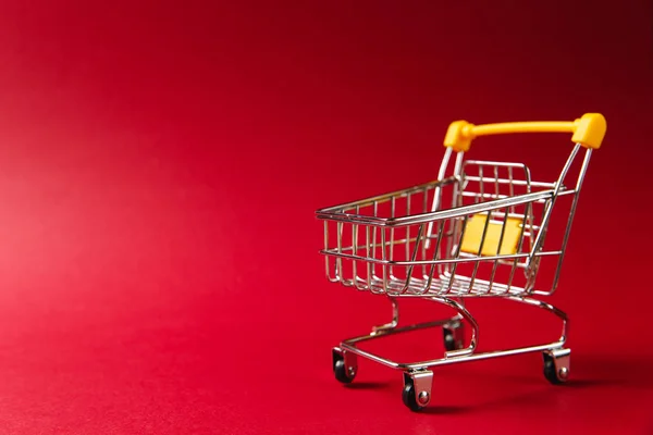 Gros plan du chariot d'épicerie de supermarché pour faire du shopping avec des roues noires et des éléments en plastique jaune sur poignée isolée sur fond rouge. Concept de shopping. Espace de copie pour la publicité — Photo