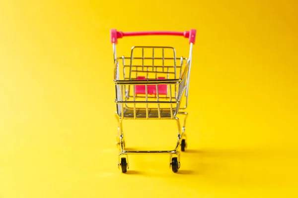 Gros plan du chariot d'épicerie de supermarché pour faire du shopping avec des roues noires et des éléments en plastique rouge sur poignée isolée sur fond jaune. Concept de shopping. Espace de copie pour la publicité — Photo