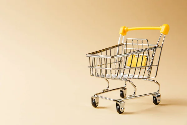 Gros plan du chariot d'épicerie de supermarché pour magasiner avec des roues noires et des éléments en plastique jaune sur poignée isolée sur fond beige. Concept de shopping. Espace de copie pour la publicité — Photo