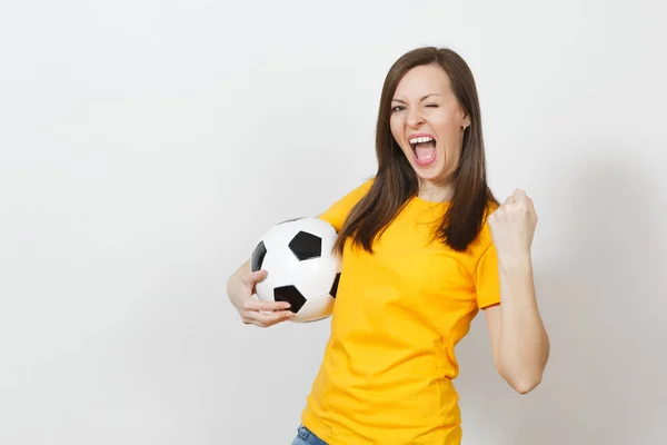 Beautiful European young woman, football fan or player in yellow uniform holding soccer ball showing winner gesture isolated on white background. Sport play football health, healthy lifestyle concept.
