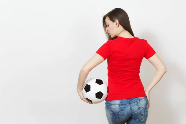 Back view beautiful European young sexy woman, football fan or player in red uniform holding classic soccer ball isolated on white background. Sport, play football, health, healthy lifestyle concept.