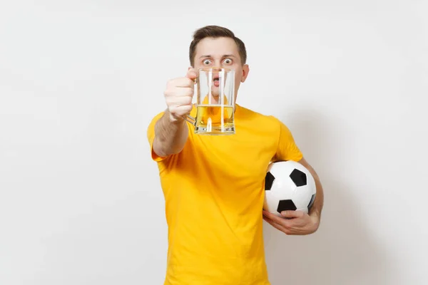 Inspirado joven divertido hombre europeo, ventilador o jugador en uniforme amarillo celebrar en la cara delantera pinta taza de cerveza, fútbol bola animar equipo de fútbol favorito aislado sobre fondo blanco. Deporte, concepto de estilo . — Foto de Stock