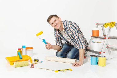 Duvar kağıdı rulo, boya silindiri, beyaz arka plan üzerinde izole yenileme daire oda için aygıtlar ile katta oturan genç adam. , Duvar kağıdı yapıştırma aksesuarları, boyama araçlarını. Onarım ev concept