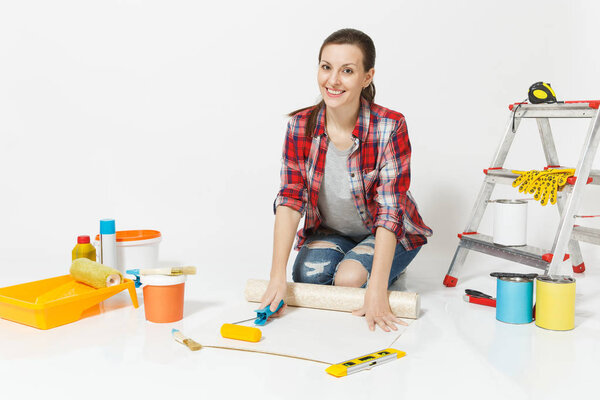 Woman in casual clothes sitting on floor with wallpaper rolls, paint roller, instruments for renovation apartment isolated on white background. Accessories for gluing, painting tools. Repair concept.