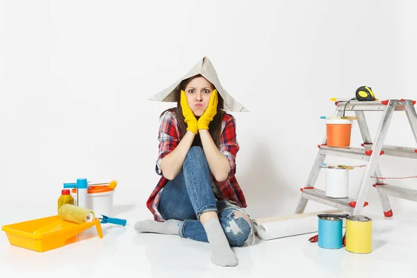 Mulher bonita em chapéu de jornal, luvas amarelas sentadas no chão com instrumentos para renovação apartamento isolado no fundo branco. Papel de parede, acessórios de colagem, ferramentas de pintura. Reparação home concept — Fotografia de Stock