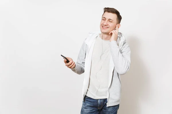 年轻英俊的男学生在 t恤衫, 蓝色牛仔裤和轻运动衫听音乐在手机上的耳机和享受在演播室白色背景。情绪的概念, 好心情. — 图库照片