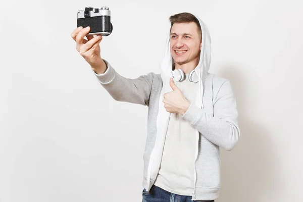 Młody przystojny student uśmiechający się człowiek w t-shirt i lekka bluza z kaptur z słuchawki fotografie sam aparat retro i pokazuje kciuk na białym tle na białym tle. Koncepcja fotografii — Zdjęcie stockowe