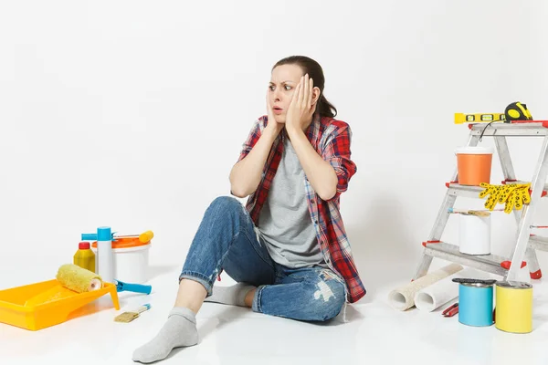 Confuso irritado cansado chocado mulher sentado no chão com instrumentos para renovação apartamento isolado no fundo branco. Papel de parede, acessórios para colar, ferramentas de pintura. Conceito de casa de reparação . — Fotografia de Stock