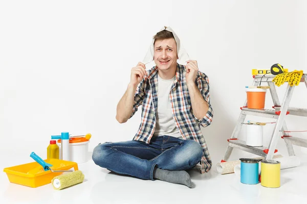 Divertido hombre sonriente feliz en sombrero de periódico sentado en el suelo con instrumentos para la renovación habitación del apartamento aislado sobre fondo blanco. Fondo de pantalla, pegar accesorios, herramientas de pintura. Reparación concepto hogar . — Foto de Stock