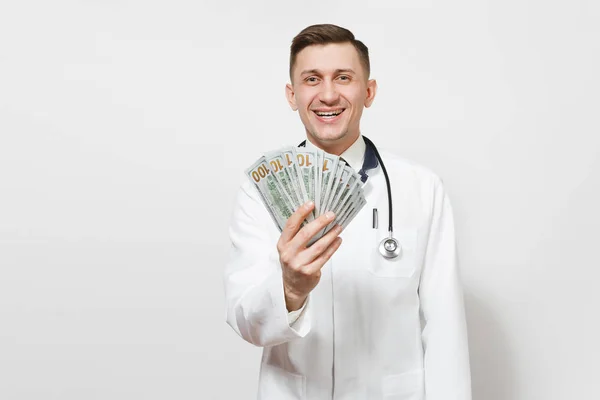 Усміхнений молодий лікар ізольований на білому тлі. Чоловік-лікар в медичній формі, стетоскоп тримає пакет доларів, банкноти, готівкові гроші. Медичний персонал, охорона здоров'я, концепція медицини . — стокове фото