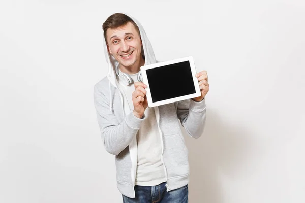 Młody przystojny człowiek uśmiechający się w t-shirt i lekka bluza z kapturem ze słuchawkami posiada komputer typu tablet pc z pustego ekranu kopia miejsce na białym tle. Koncepcja technologii. — Zdjęcie stockowe