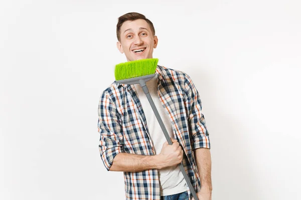 Joven ama de llaves feliz sonriente con camisa a cuadros sosteniendo y barriendo con escoba verde aislado sobre fondo blanco. Hombre haciendo tareas domésticas. Copia espacio para la publicidad. Concepto de limpieza . — Foto de Stock