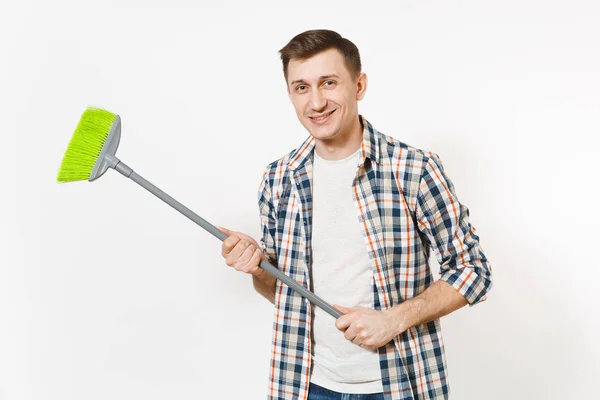 Joven ama de llaves feliz sonriente con camisa a cuadros sosteniendo y barriendo con escoba verde aislado sobre fondo blanco. Hombre haciendo tareas domésticas. Copia espacio para la publicidad. Concepto de limpieza . — Foto de Stock