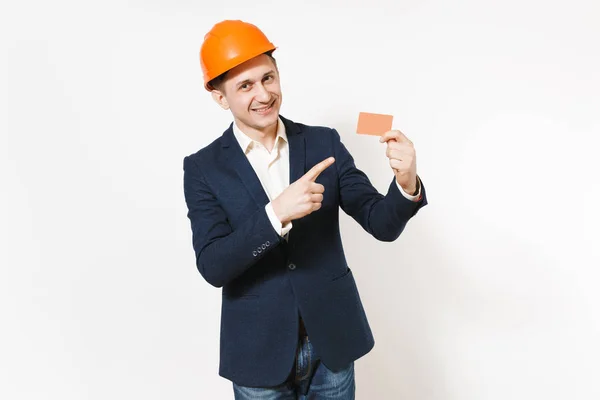 Joven hombre de negocios guapo sonriente en traje oscuro, protector naranja hardhat señalando el dedo índice en la tarjeta de crédito en blanco aislado sobre fondo blanco. Trabajador masculino para publicidad. Concepto empresarial . — Foto de Stock
