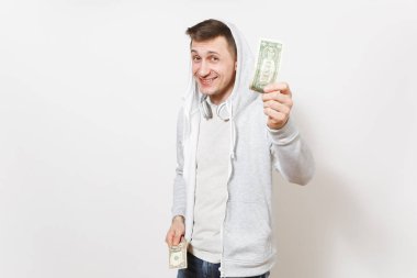 Öğrenci tişört içinde mutlu eğlence gülümseyen yakışıklı genç adam, kulaklık ile hood ile hafif kazak bir dolarlık banknot tutar ve beyaz arka plan üzerinde izole kamera için gösterir. Duygular kavramı