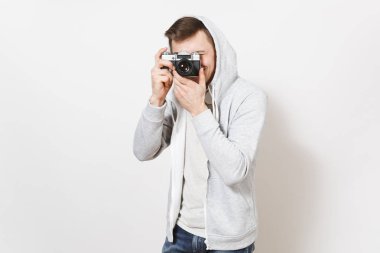 Genç yakışıklı gülümseyen erkek öğrenci tişört ve kulaklık ile hood ile hafif kazak beyaz arka plan üzerinde izole retro kamerada fotoğraf çeker. Genel kavram-in fotoğraf, hobi