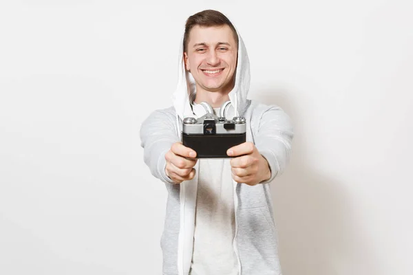 Der junge, gut aussehende lächelnde Student in T-Shirt und hellem Sweatshirt mit Kapuze und Kopfhörer fotografiert sich selbst mit der Retro-Kamera isoliert auf weißem Hintergrund. Konzept der Fotografie, Hobby — Stockfoto