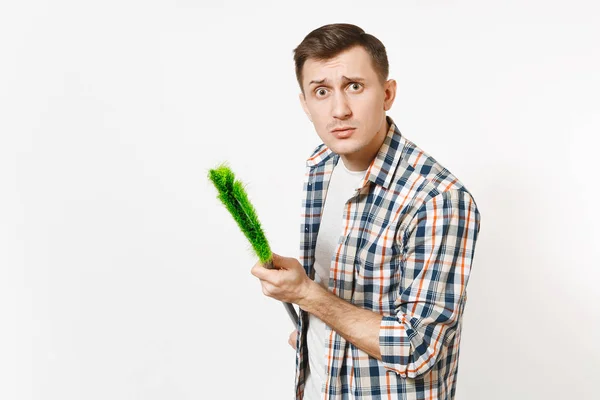 Joven y divertido ama de llaves con camisa a cuadros sosteniendo y barriendo con escoba verde aislada sobre fondo blanco. Hombre haciendo tareas domésticas. Copia espacio para la publicidad. Concepto de limpieza . — Foto de Stock