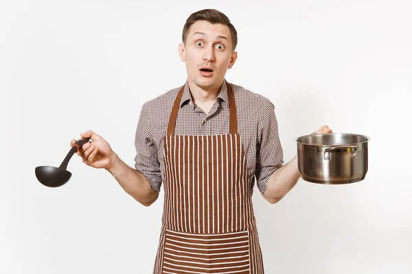 Чоловік шеф-кухар в смугастому коричневому фартусі, що тримає срібний нержавіючий глянсовий алюмінієвий порожній рагу, сковорідку або горщик, ковдру ізольовано на білому тлі. Чоловік-домогосподарка або працівник. Кухонне начиння, концепція посуду . — стокове фото
