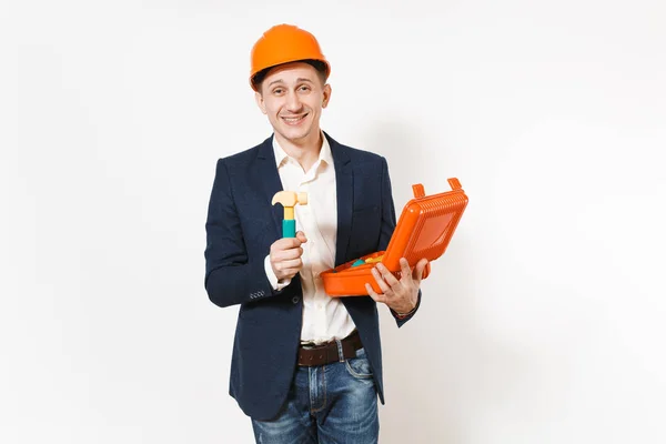 Joven hombre de negocios sonriente en traje oscuro, casco de construcción protectora con funda abierta con instrumentos o caja de herramientas y martillo de juguete aislado sobre fondo blanco. Trabajador masculino para publicidad . — Foto de Stock