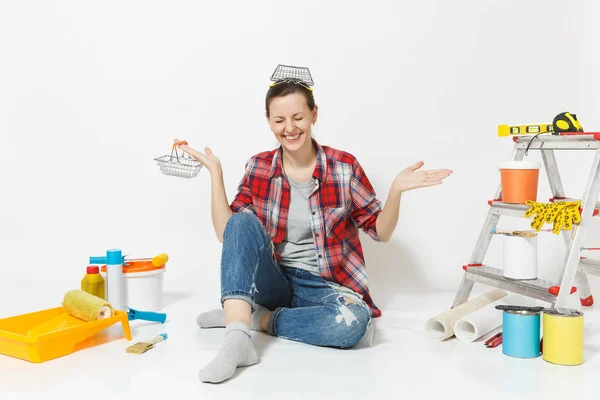 Donna tiene cestini metallici per la spesa, si siede al piano con strumenti per la ristrutturazione appartamento isolato su sfondo bianco. Carta da parati, accessori, strumenti per la pittura. Riparazione concetto di casa . — Foto Stock