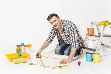 Rulo duvar kağıdı, ölçü birimi teyp, kalem, yenileme daire oda için aygıtlar ile katta oturan genç adam beyaz arka plan üzerinde izole. Aksesuarlar, boyama araçlarını yapıştırma. Onarım ev concept