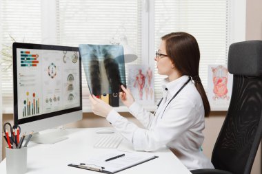 Bilgisayarda, hastanede ışık Office x-ışını akciğerler, fluorography, roentgen tutarak çalışma kadın doktor masada oturuyor. Tıbbi önlük, stetoskop Oda danışmanlık içinde kadın. Tıp kavramı.