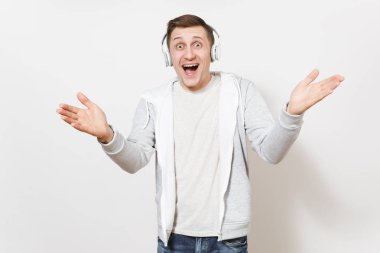 Genç yakışıklı gülümseyen adam öğrenci tişört ve ışık kazak sürpriz elinde beyaz arka plan üzerinde izole yayılır ve beyaz kablosuz kulaklık ile müzik dinlemek. Duygular kavramı