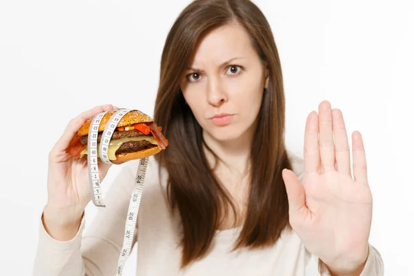 Close up mulher segura em mãos hambúrguer com fita métrica alfaiate em torno isolado no fundo branco. Nutrição adequada ou fast food clássico americano. Espaço de cópia para propaganda. Área publicitária . — Fotografia de Stock