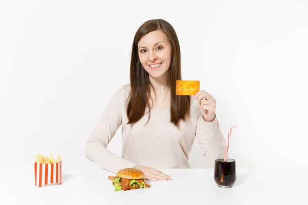 Szczęśliwa kobieta siedzi przy stole z karty kredytowej, burger, frytki, cola w szklanej butelce na białym tle. Prawidłowe odżywianie lub klasyczny amerykański fast food. Reklama obszar z miejsca kopii — Zdjęcie stockowe