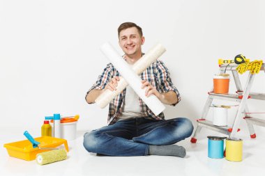 Çapraz rulo duvar kağıdı, beyaz arka plan üzerinde izole yenileme daire için aygıtlar ile katta oturan rahat kıyafetler gülümseyen adam. Aksesuarlar, boyama araçlarını yapıştırma. Onarım kavramı.