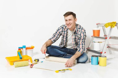 Duvar kağıdı rulo, kalem, beyaz arka plan üzerinde izole yenileme daire oda için aygıtlar ile katta oturan genç adam. , Duvar kağıdı yapıştırma aksesuarları, boyama araçlarını. Onarım ev concept.