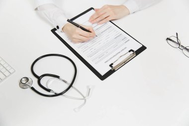 Doktor hastanede ışık ofiste tıbbi belgeleri doldurma çalışma eller. Yazma kağıt Pano, stetoskop Oda danışmanlık içinde tablo üzerinde bir kadın. Tıp kavramı. Üstten Görünüm. Kopya alanı.
