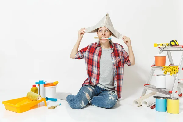 Nő ül a padló kefével a szájban, eszközök felújítás apartman elszigetelt fehér background újság kalapban. Tapéta, kiegészítők, ragasztás, festés eszközök. Javítás otthon koncepció. — Stock Fotó
